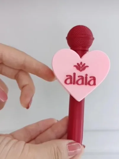Adaptador en forma de corazón rosado con logo rojo sobre un soporte del mismo tono rojo