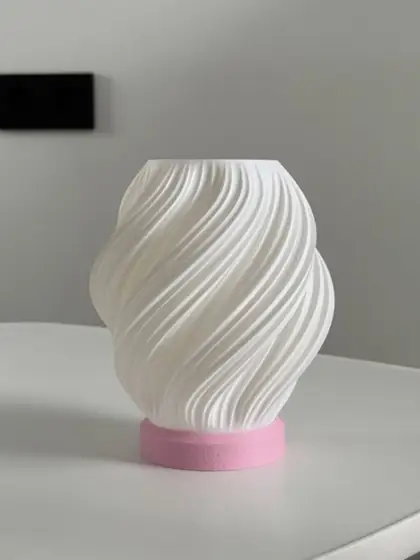 Lámpara de pantalla blanca con líneas en espiral y base rosada sobre una mesa blanca