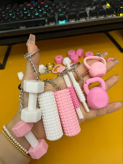 Varios llaveros de gimnasio en blanco y rosado con formas de mancuernas, rodillos y pesas rusas